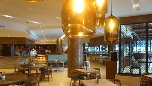 Un restaurant spacieux, doté de nombreuses tables et chaises, d’un grand luminaire décoratif et offrant une vue sur la cuisine.