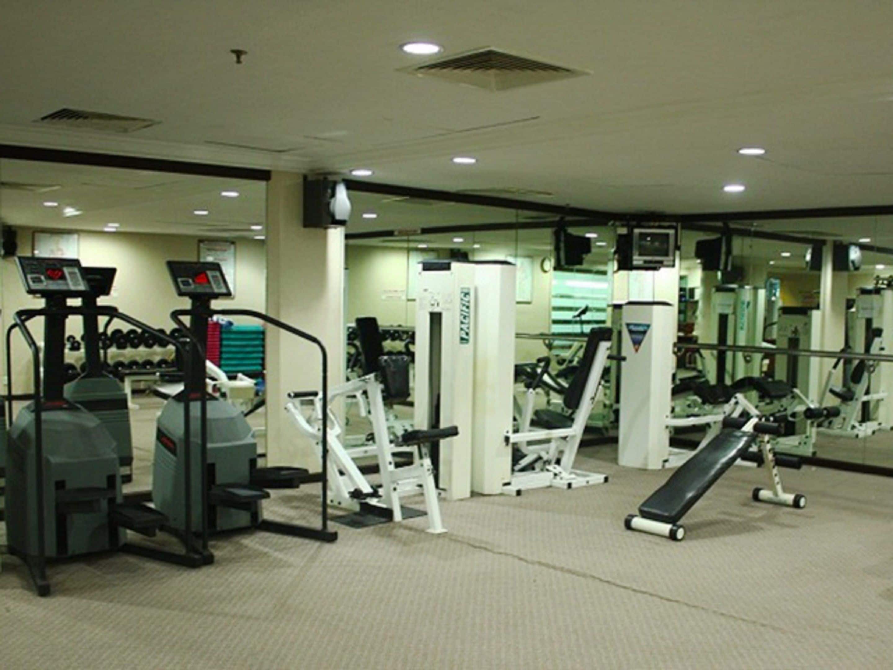 A gym with cardio machines, weight training equipment, and a mirrored wall.