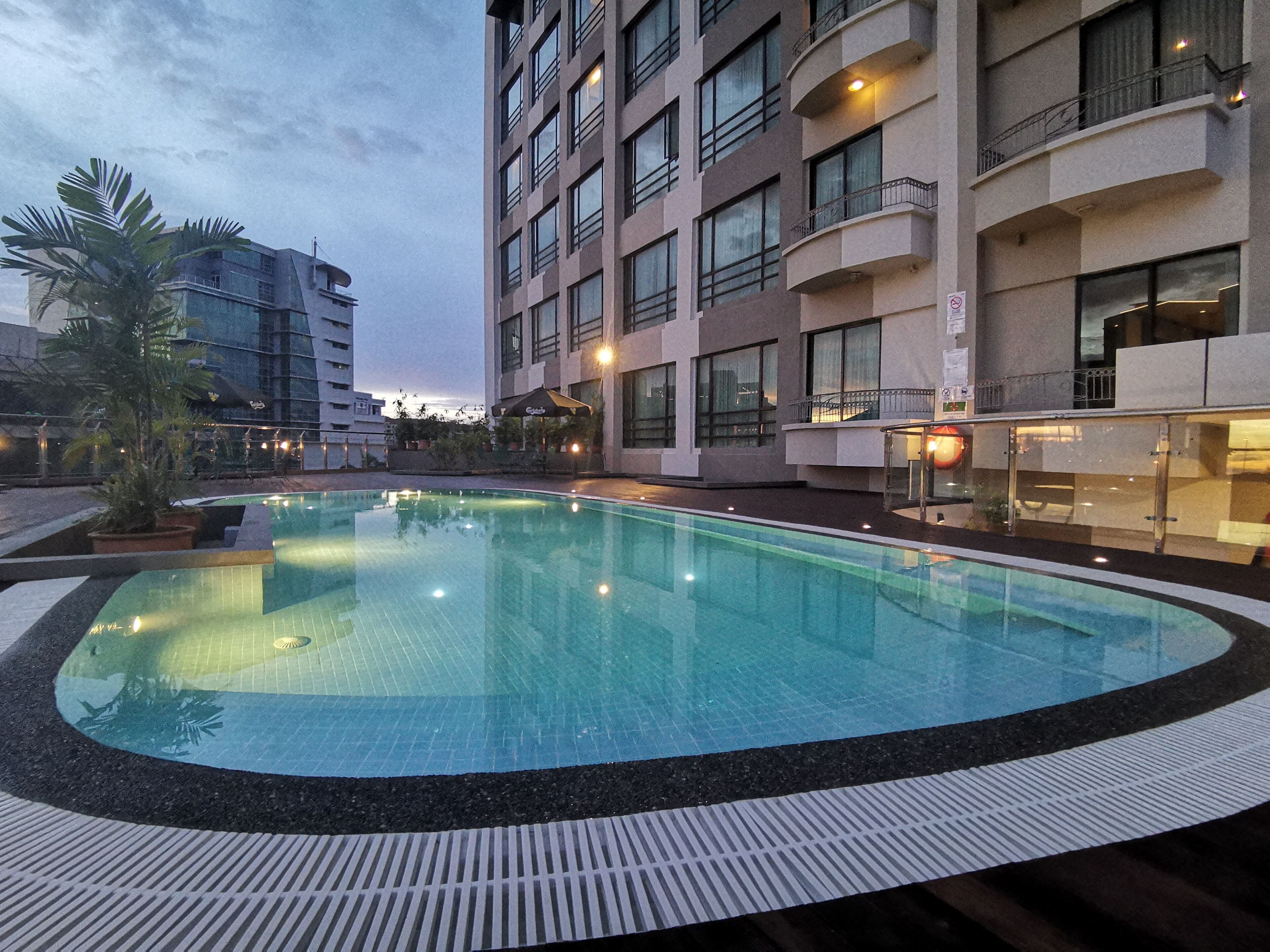 Uma piscina com borda azulejada, rodeada por um edifício com várias varandas e janelas.