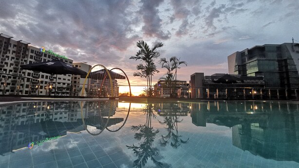 Une piscine avec vue sur le coucher de soleil, des bâtiments modernes et des palmiers.