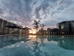 En swimmingpool med udsigt til solnedgang, moderne bygninger og palmer.