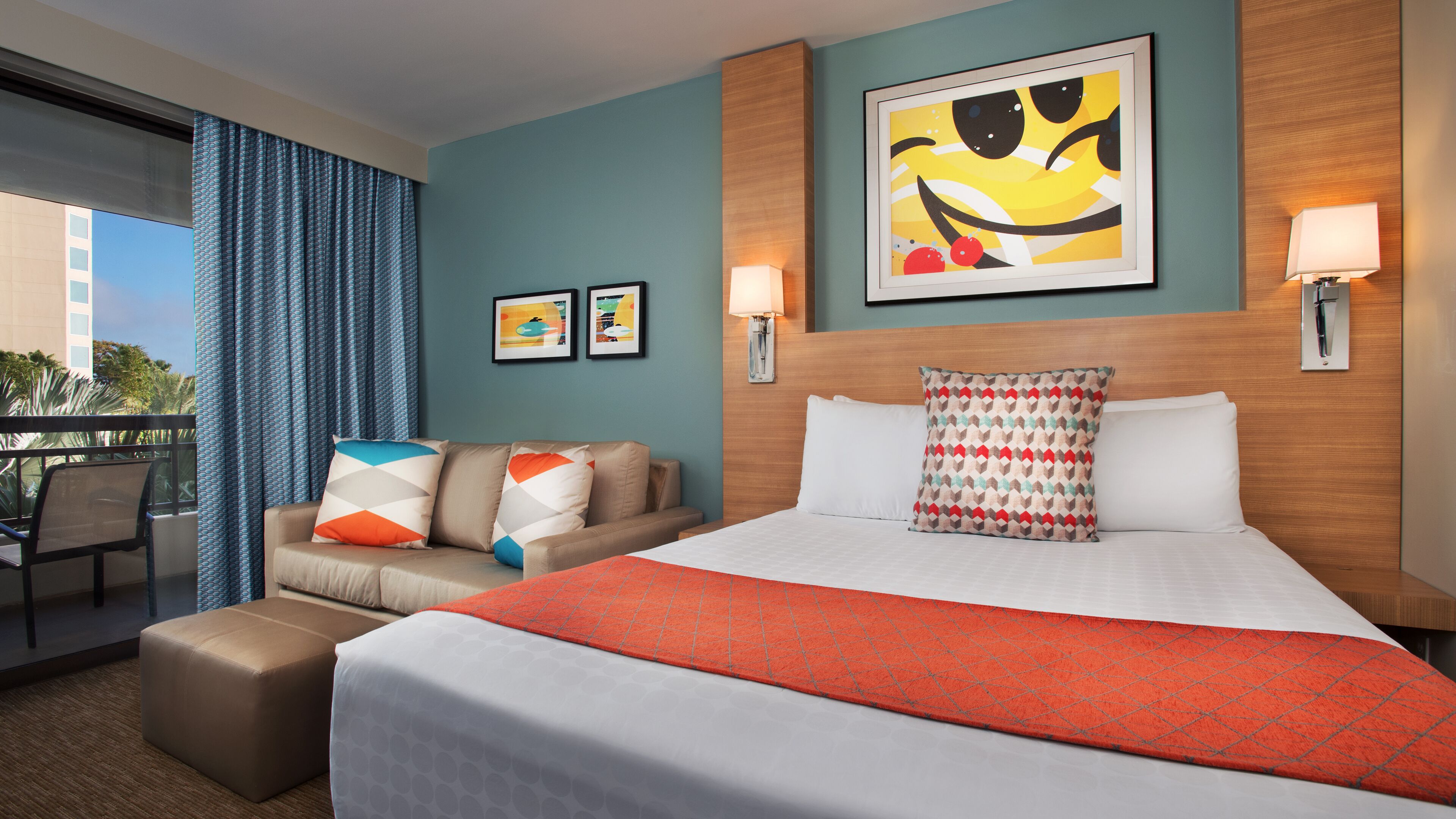 Una habitación de hotel con cama, sofá, una mesita y balcón con cortinas.