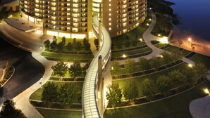 A multi-story hotel with a curved facade, illuminated windows, and a landscaped garden with pathways. - Bay Lake Tower at Disney's Contemporary Resort (Lake Buena Vista)