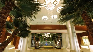 A spacious lobby with a modern chandelier, palm trees, and a reception desk. - Bay Lake Tower at Disney's Contemporary Resort (Lake Buena Vista)
