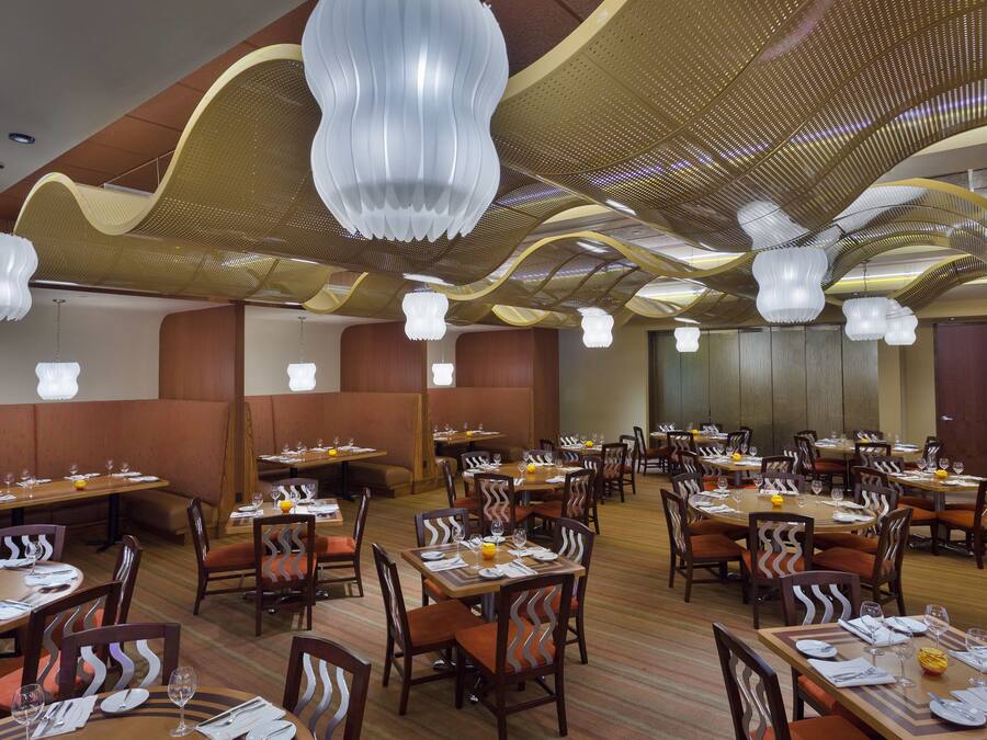 Un ristorante spazioso con diversi tavoli e posti a sedere, caratterizzato da un design moderno del soffitto e illuminazione d'ambiente.