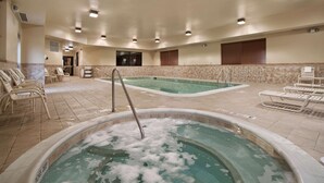 Una amplia piscina interior con un jacuzzi al frente, rodeada de sillones de descanso y suelo de baldosas.