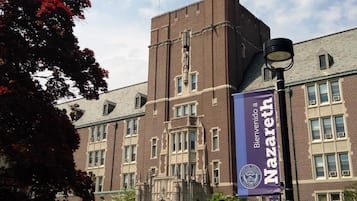 En historisk byggnad med en framträdande entré, ett högt torn och banderoller med Nazareth Colleges logotyp.