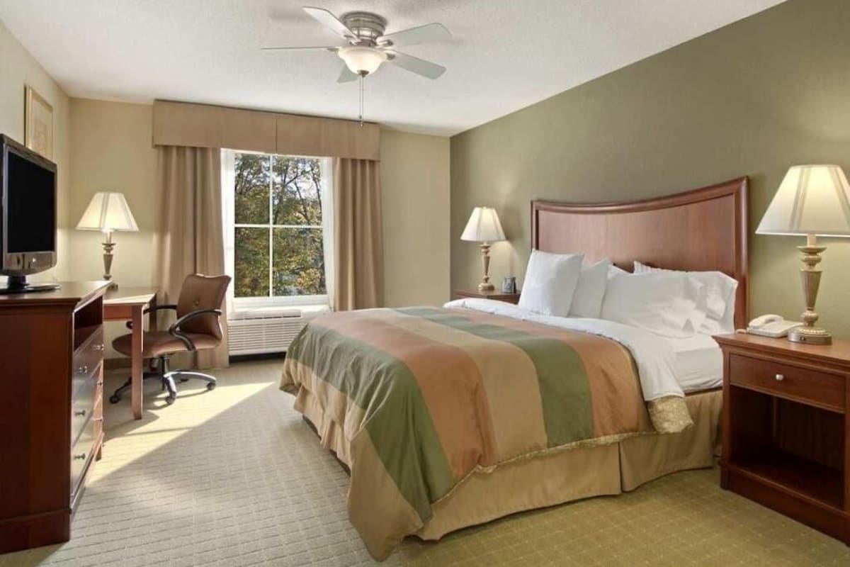 Une chambre d’hôtel équipée d’un lit, d’un bureau, d’une chaise et d’un ventilateur de plafond.
