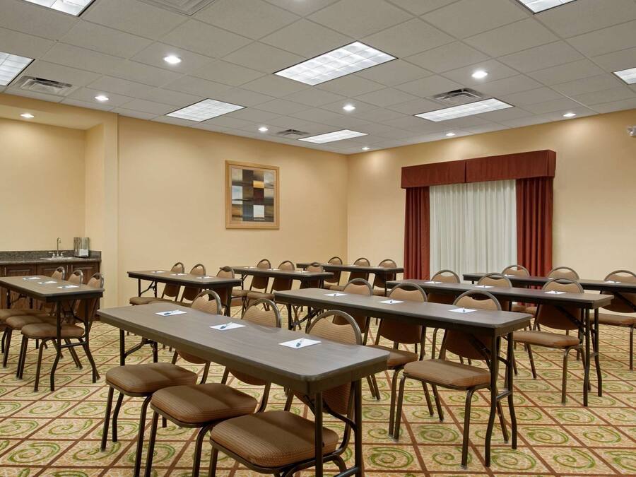 A conference room with multiple tables and chairs, a kitchenette, and a large window with curtains.