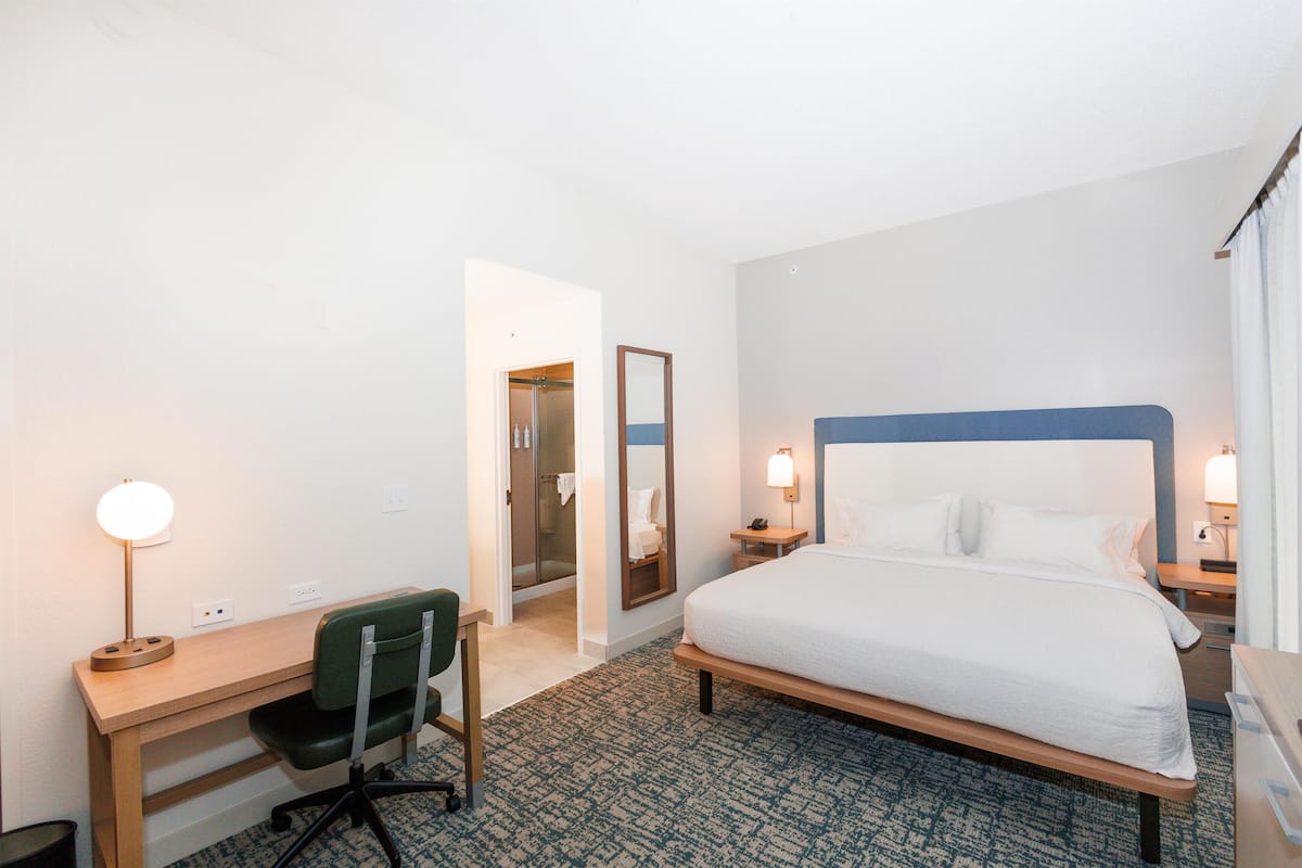 Habitación de hotel con cama, escritorio, silla y zona de ducha.