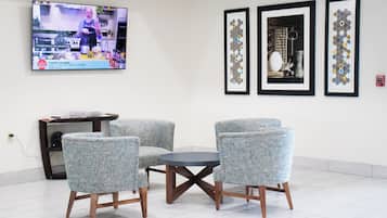 A modern room with a TV displaying a cooking show, a round table, four upholstered chairs, and three framed artworks on the wall.