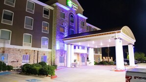 Un hotel Holiday Inn Express con entrada cubierta, estacionamiento y una zona ajardinada con arbustos.
