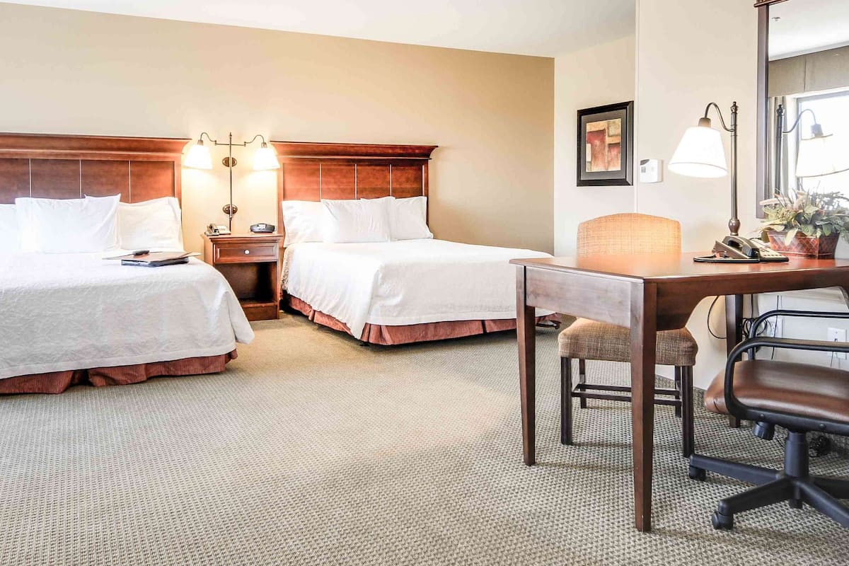 A hotel room with two beds, a desk with a chair, a lamp, and a window.