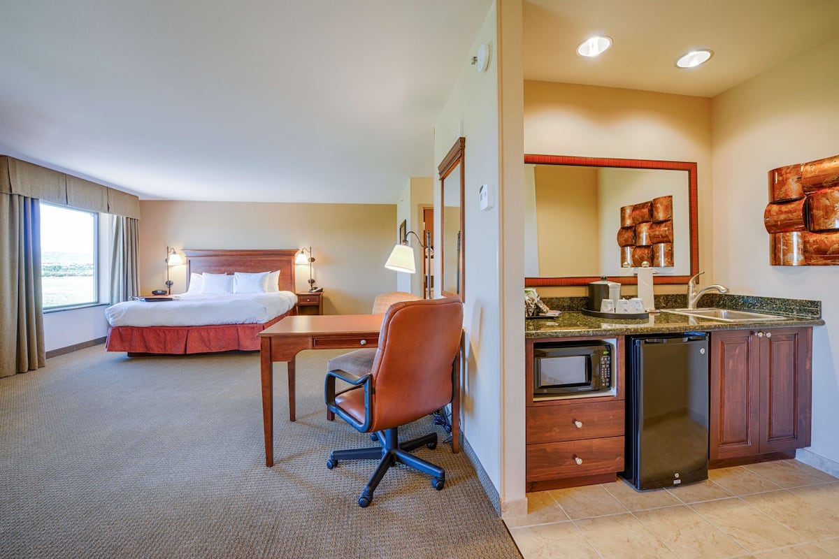 A hotel room with a bed, desk, chair, kitchenette, and a large mirror.