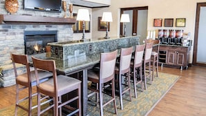 A spacious bar area with a stone wall, a flat-screen TV, and a fireplace. There are several bar stools and a long bar counter. - Hampton Inn & Suites Pinedale (Pinedale)