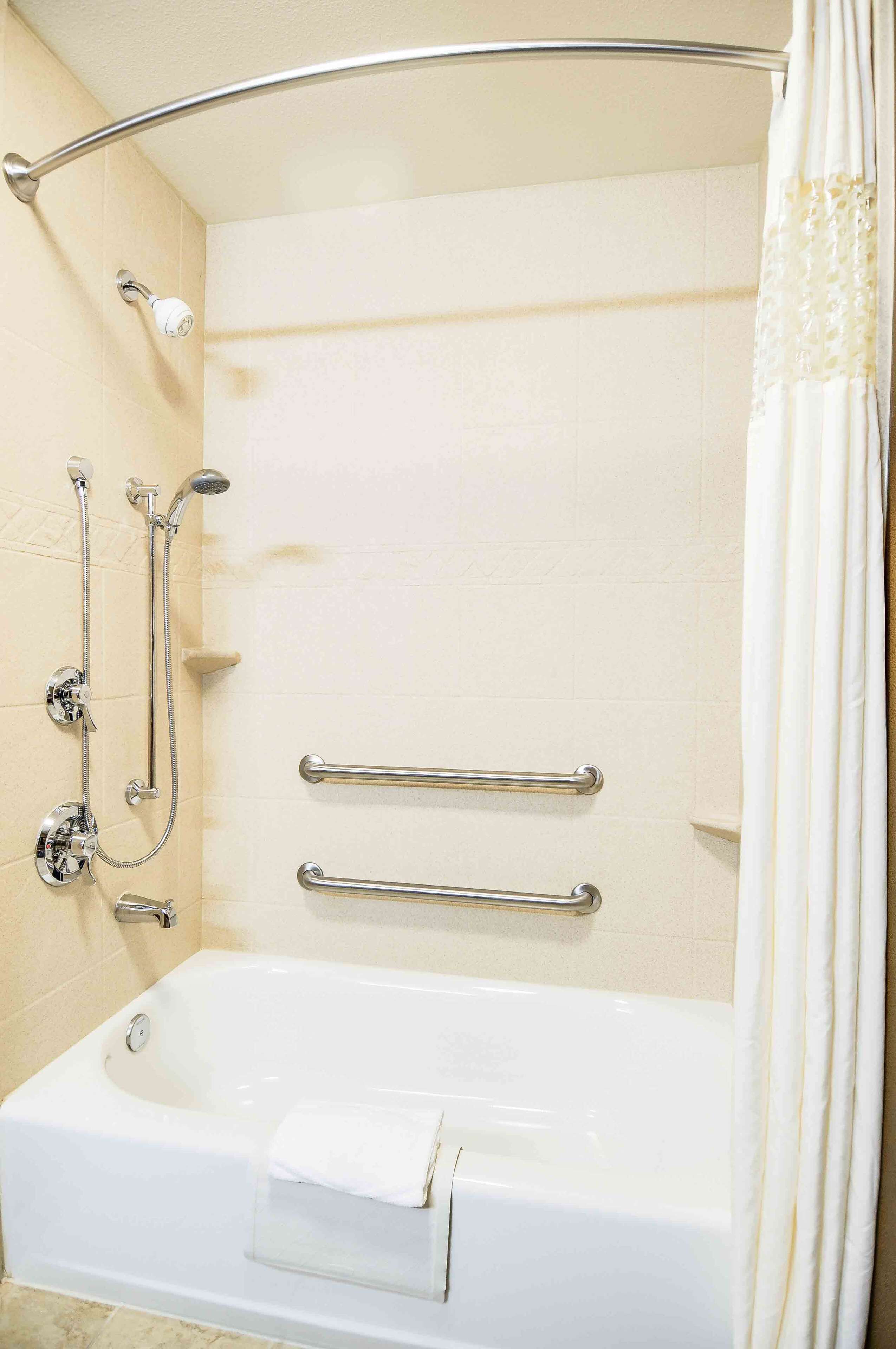 A modern bathroom with a bathtub, shower, and grab bars.