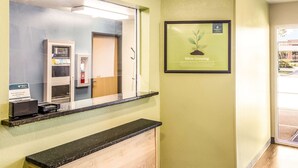 A reception area with a counter, a framed sign on the wall, and a vending machine. - WoodSpring Suites Houston Baytown (Baytown)