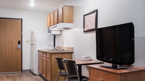 A compact kitchen with wooden cabinets, a refrigerator, a microwave, and a small dining table with two chairs. - WoodSpring Suites Houston Baytown (Baytown)