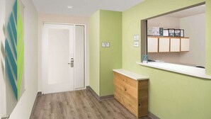 Un pasillo con suelo de madera, pared verde, puerta blanca y un mostrador con espejo y diplomas enmarcados.