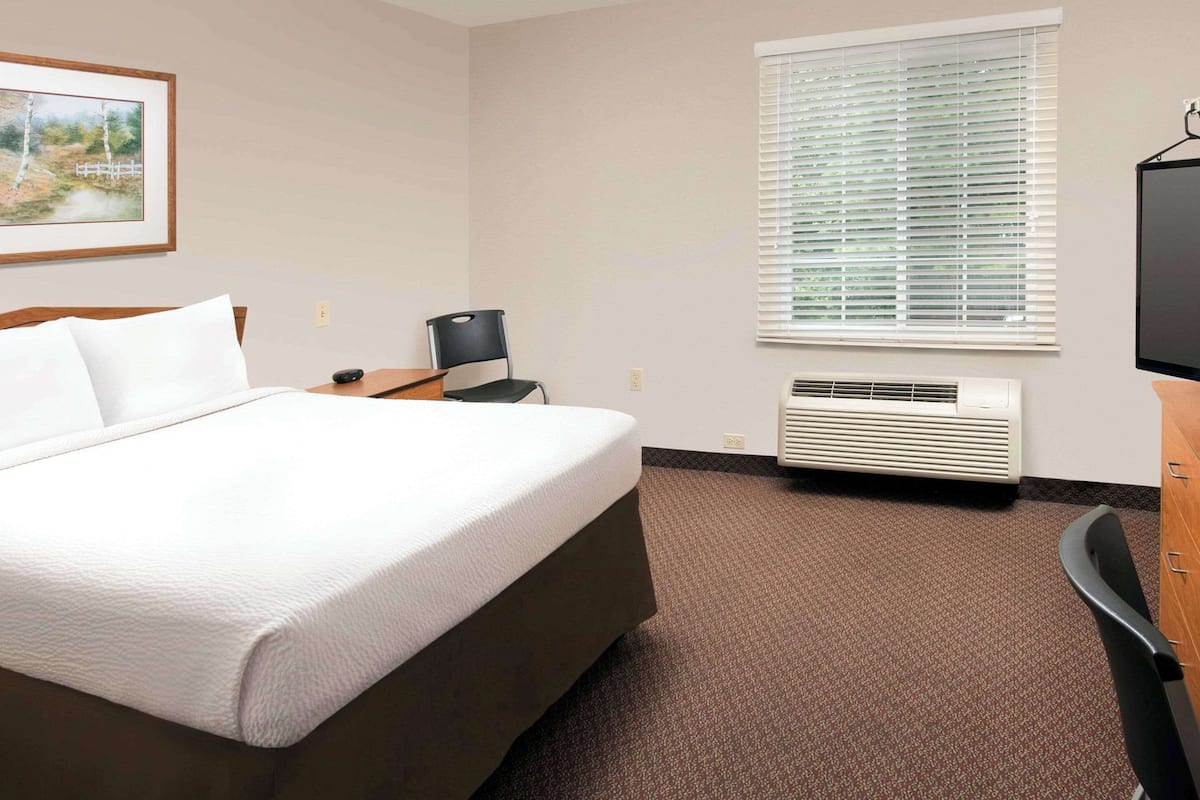 A hotel room with a bed, a desk, a chair, a television, and a window with blinds.