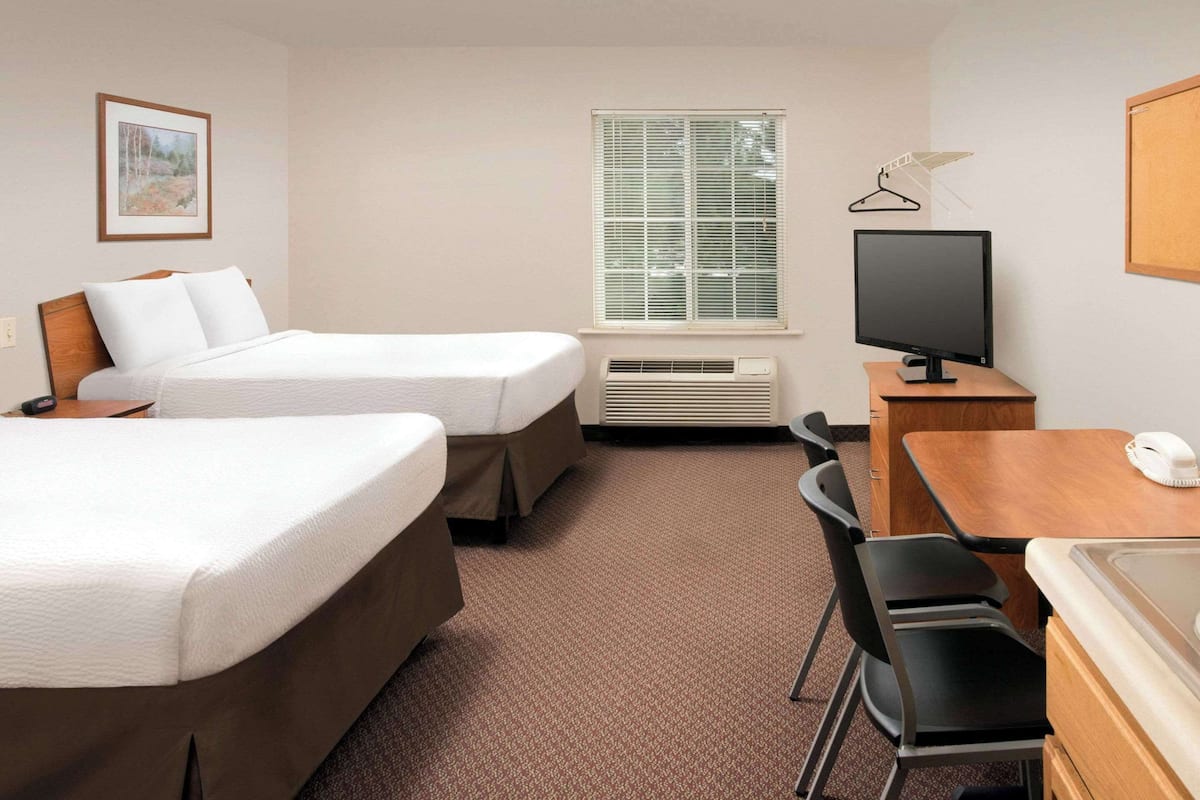 A hotel room with two beds, a desk with a computer, a chair, a TV, and a window with blinds.
