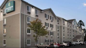 A multi-story hotel with a sign reading "Woodspring Suites". There are several cars parked in front, and the building has multiple windows and balconies.