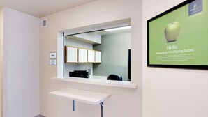 A reception area with a counter, a sign indicating an office, and a framed welcome sign. - WoodSpring Suites Cincinnati Fairfield (Fairfield)