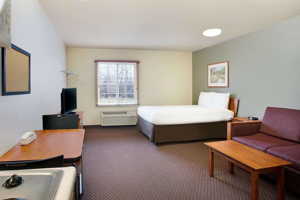 Une chambre d’hôtel comprenant un lit, un canapé, un bureau avec un téléphone, une télévision et une fenêtre avec des stores.