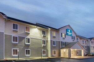 Un hotel de varios pisos con un cartel que dice Woodspring Suites. Cuenta con un estacionamiento y una entrada cubierta.
