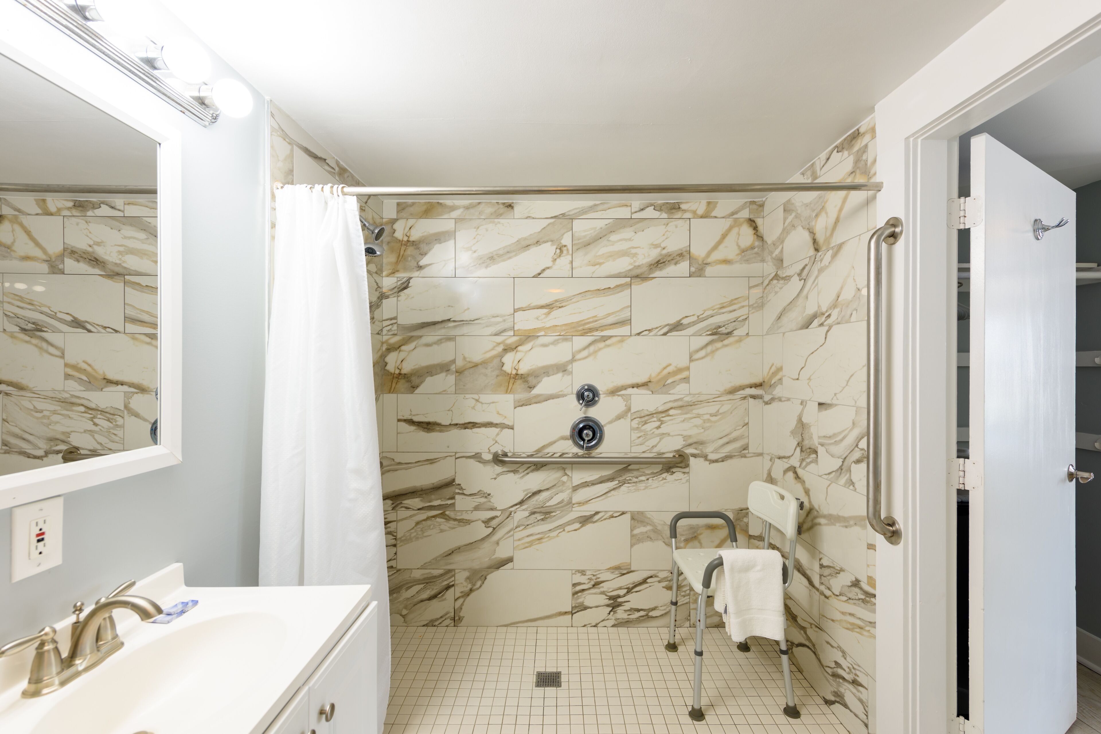 A bathroom with a marble wall, a sink, a shower, and a wheelchair-accessible bench.