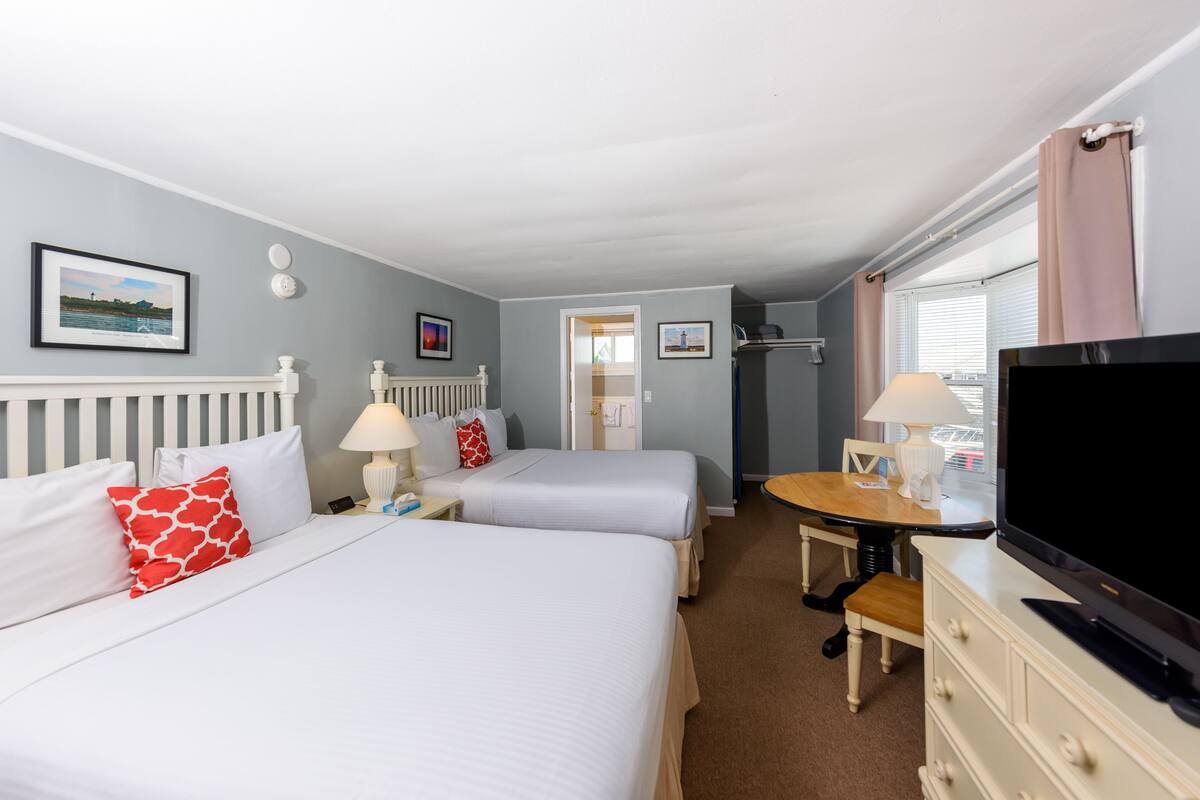 A hotel room with two beds, a TV, a desk, and a window with curtains.