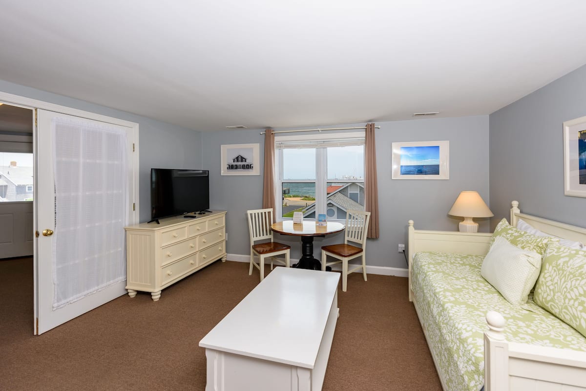 A hotel room with a bed, a TV, a dining table with chairs, a window with a view, and a door.