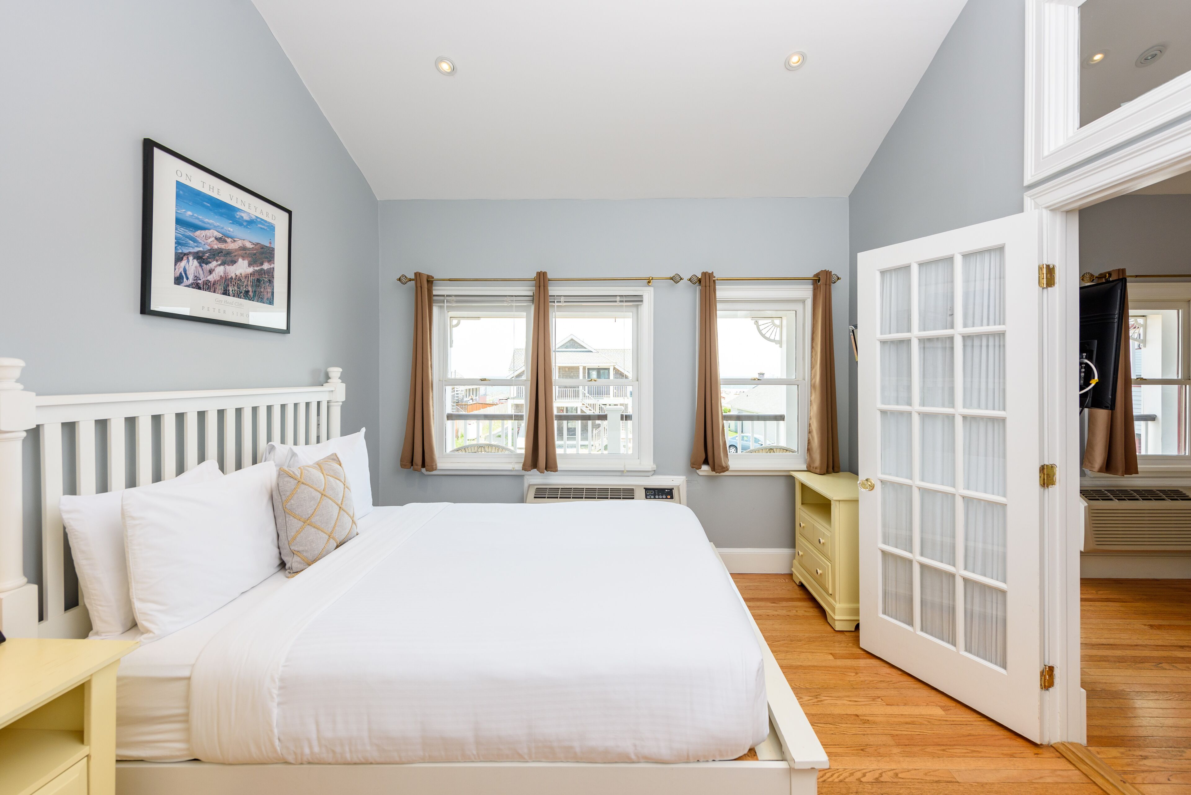 A bedroom with a bed, a nightstand, a dresser, and a door leading to another room.