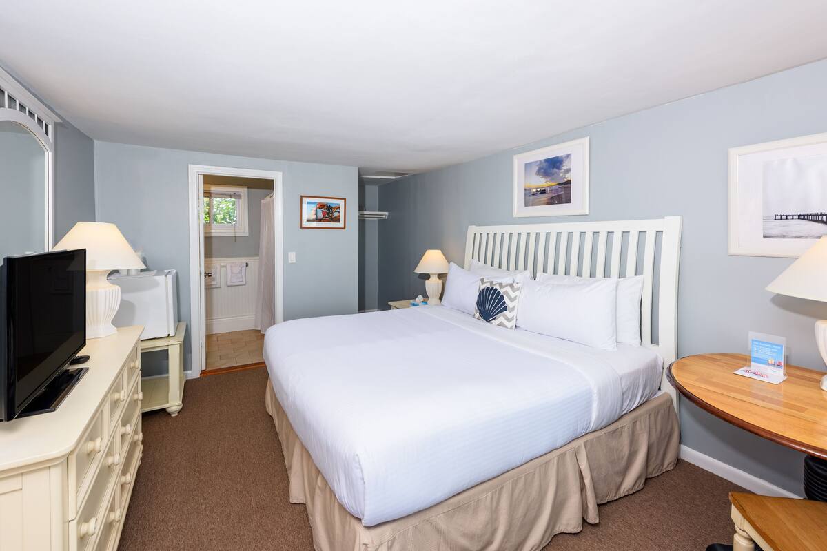 A hotel room with a large bed, a television, a desk, and a window.