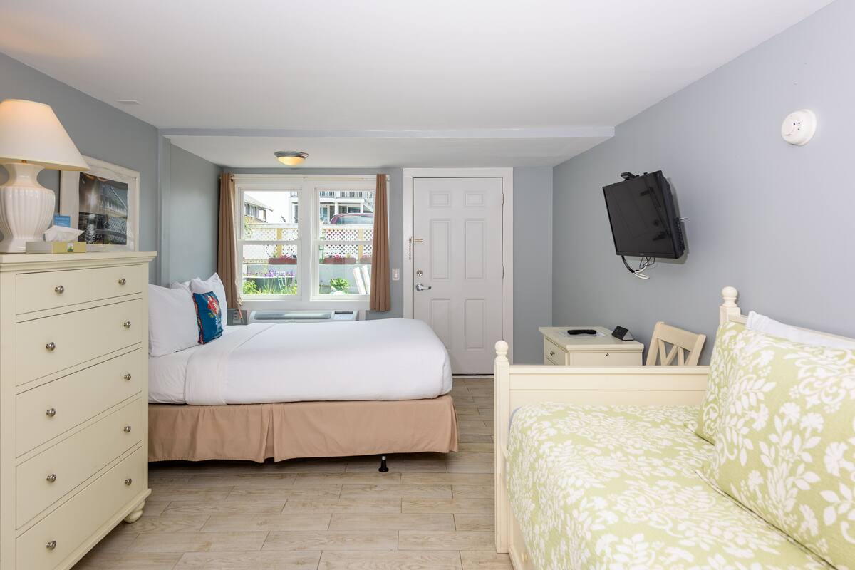 A bedroom with a bed, dresser, bedside table, and a television mounted on the wall.
