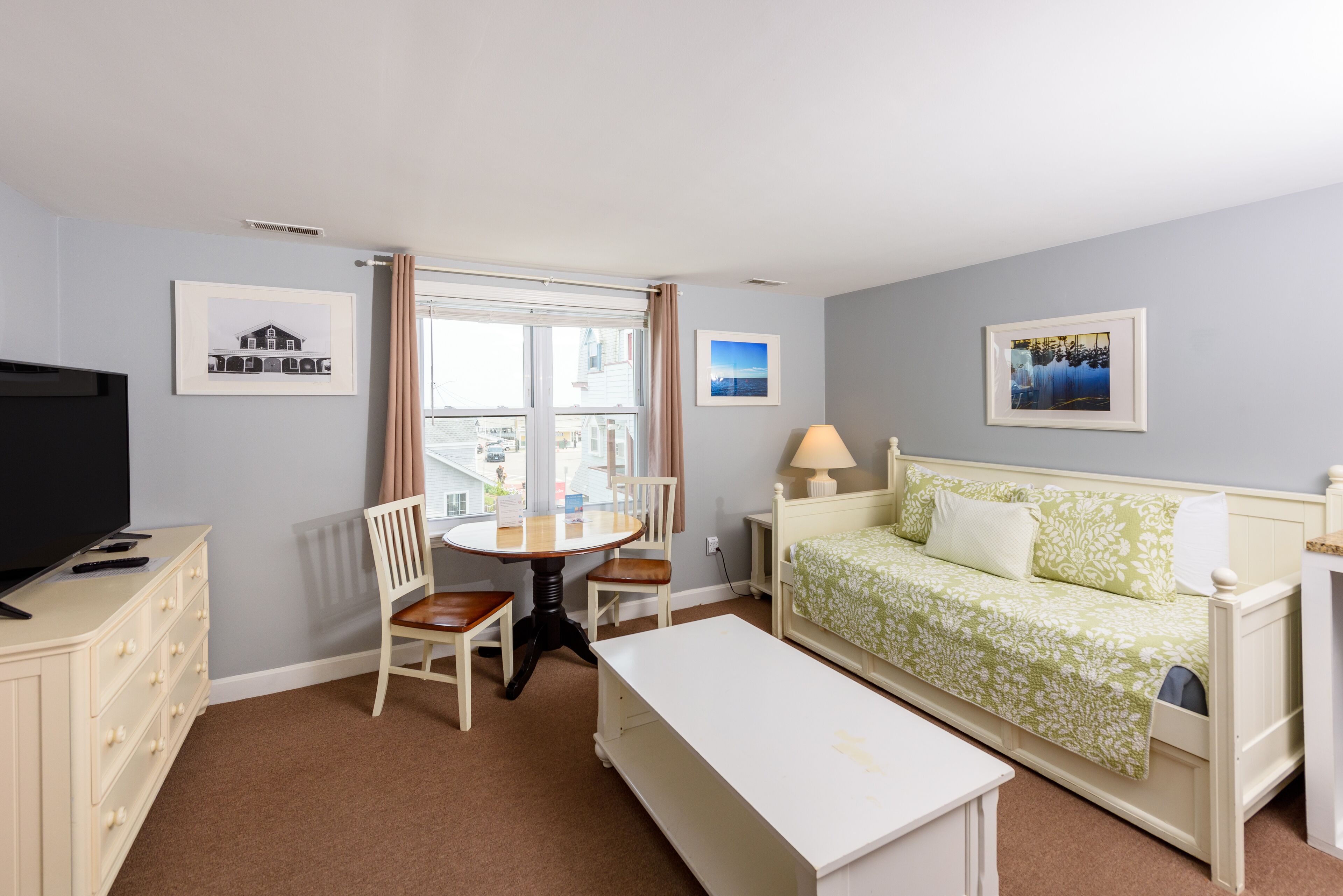 Una habitación de hotel con cama, escritorio, silla, televisor y ventana con cortinas.