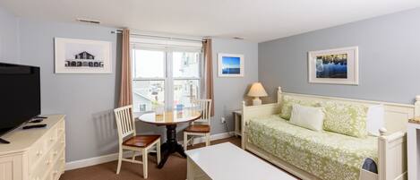 Una habitación de hotel con cama, escritorio, silla, televisor y ventana con cortinas.