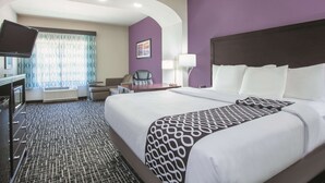 Une chambre d’hôtel avec un grand lit, un bureau avec une chaise, une télévision et une fenêtre avec des rideaux à motifs.
