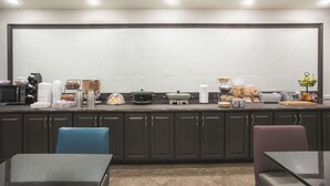 Une cuisine moderne avec des meubles de couleur sombre, une grande fenêtre et divers appareils de cuisine et ustensiles disposés sur le plan de travail.