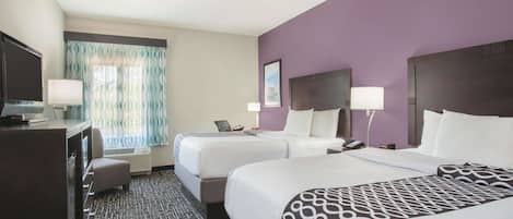 A hotel room with two beds, a desk, and a television.