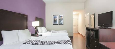 A hotel room with two beds, a TV, a desk with a lamp, and a dresser.