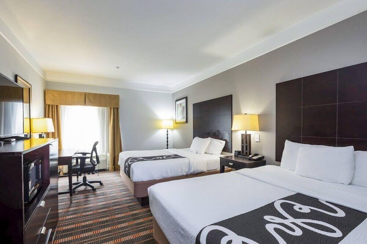 A hotel room with two beds, a desk, a chair, a TV, and a large window with curtains.