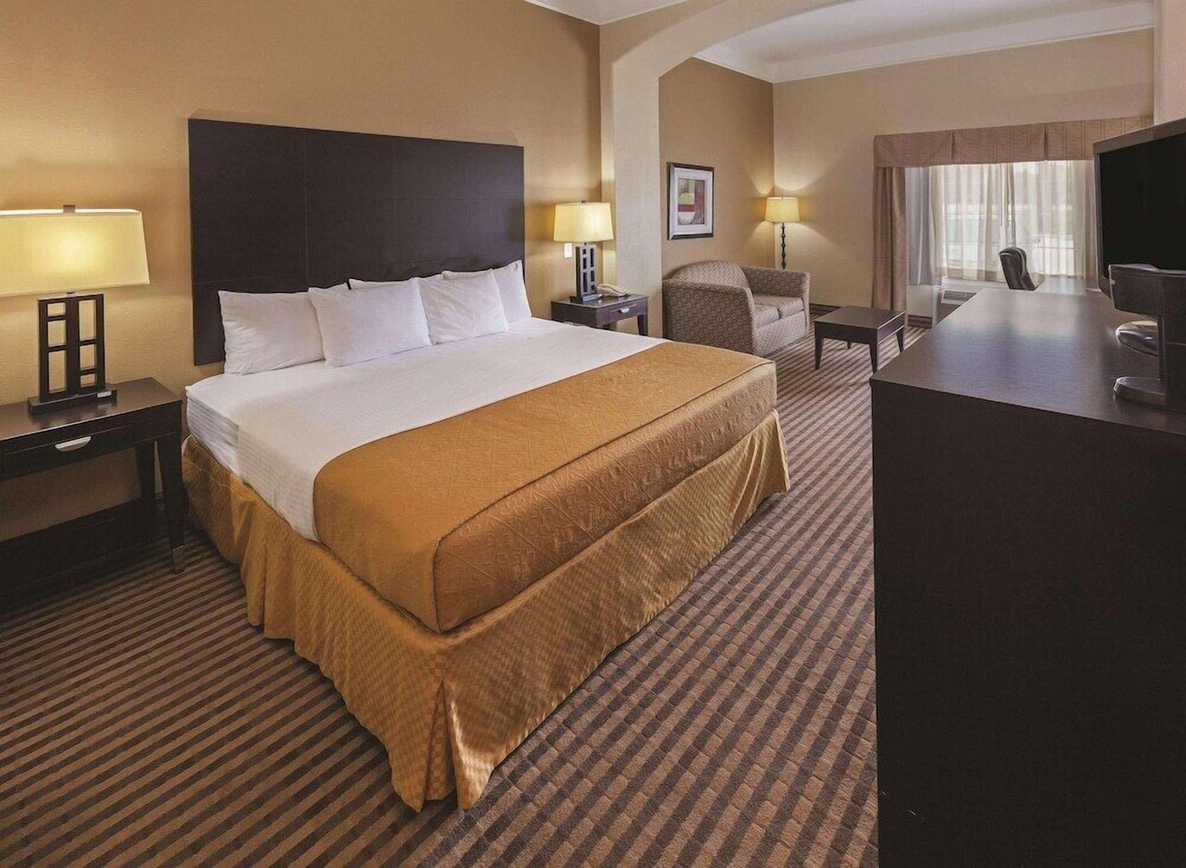 A hotel room with a large bed, a desk, a chair, and a television.