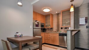 A compact kitchen with wooden cabinets, stainless steel appliances, and a dining area with a table and chairs.