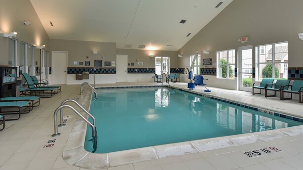 An indoor swimming pool with clear lane markings, safety signs, and lounge chairs along the sides.