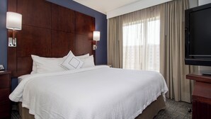 A hotel room with a large bed, a TV, and a window with curtains.