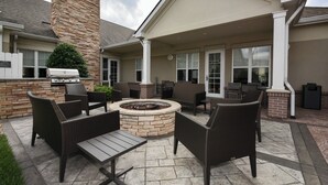 An outdoor patio area with a stone fire pit, wicker furniture, and a barbecue grill.