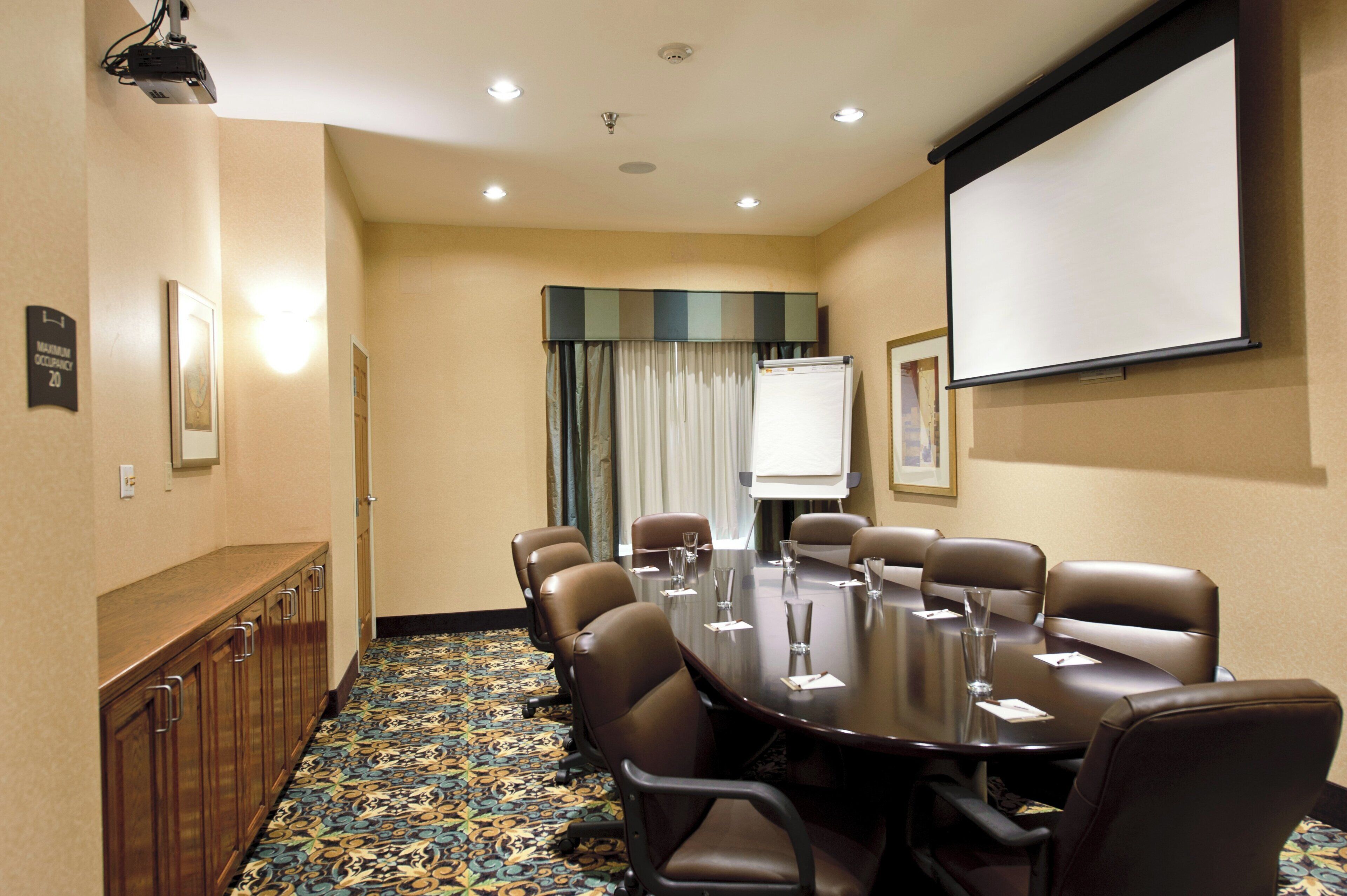 Un salón de conferencias con una larga mesa, sillas, una pantalla de proyector y una pizarra.