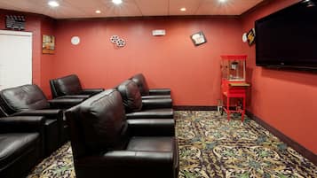 A room with leather reclining chairs, a red wall, a patterned carpet, and a television screen.