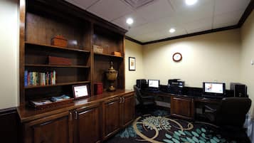 A room with a wooden desk, two computer monitors, a bookshelf, and a patterned carpet.